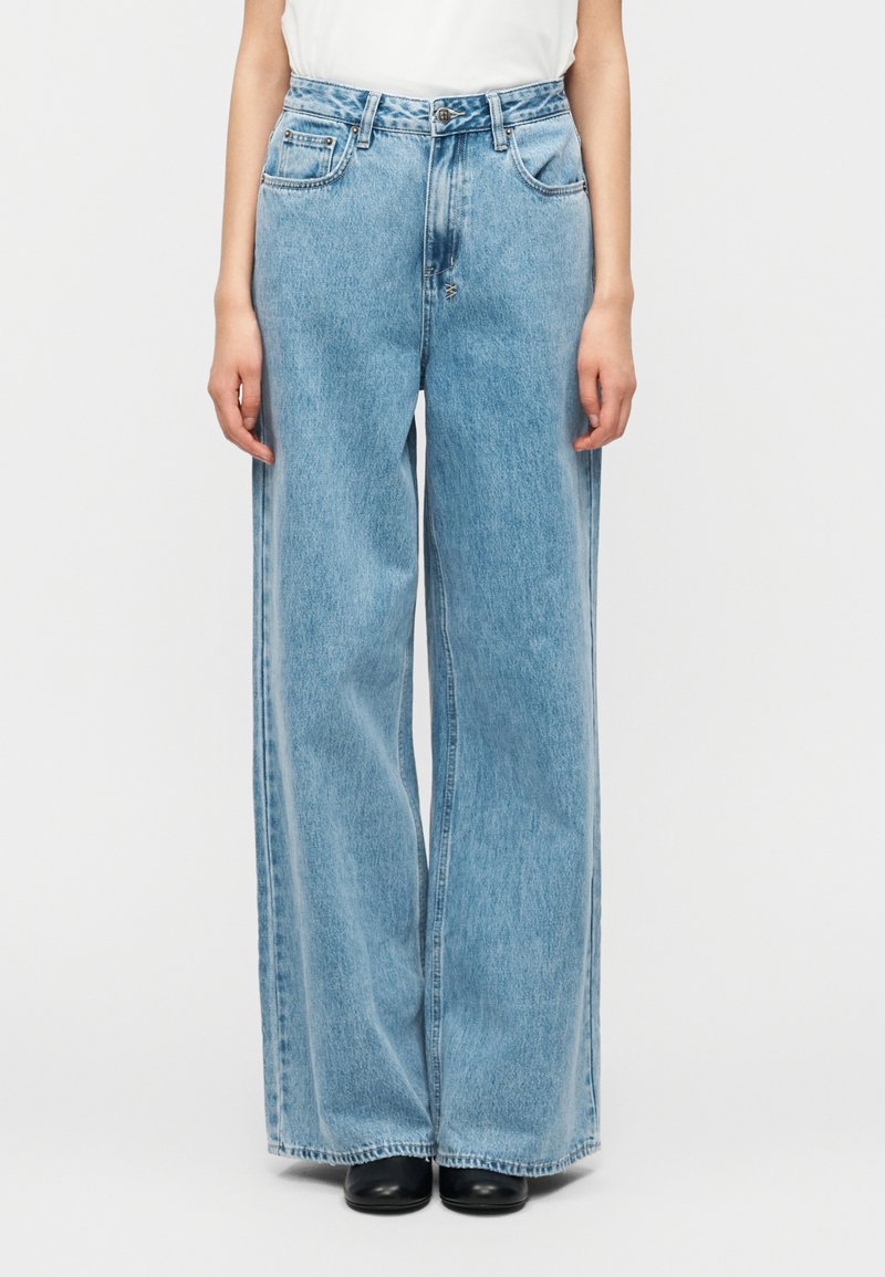 Φαρδιά τζιν παντελόνια σε ανοιχτό γαλάζιο χρώμα, κατασκευασμένα από ντένιμ, με ψηλή μέση, εμπρόσθιες τσέπες και διακριτικό ξεθώριασμα κατά μήκος των ποδιών.
