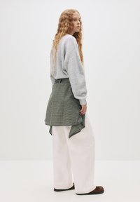 Szary, oversize'owy sweatshirt, zielona kraciasta narzuta i białe spodnie typu wide-leg. Miękkie tekstury; brązowe buty wsuwane z gumową podeszwą.