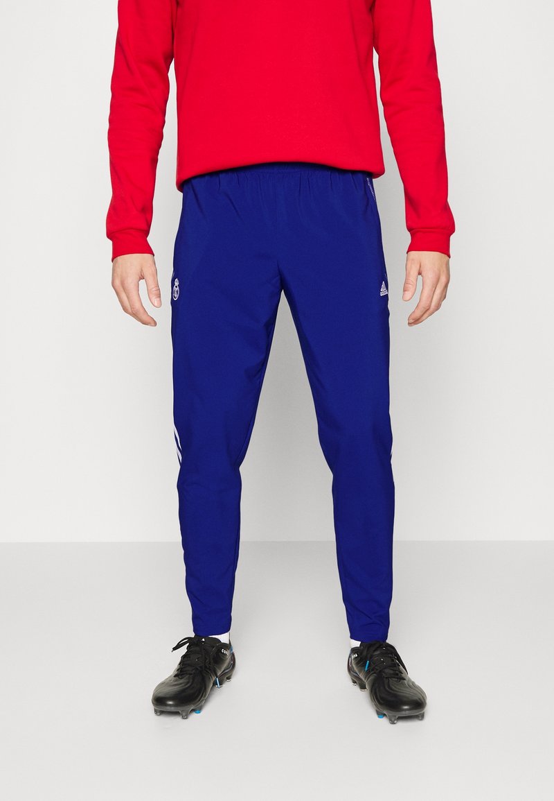 Niebieskie dresowe spodnie z elastycznym pasem i logo Adidas, połączone z czerwonymi koszulami z długim rękawem i czarnymi korkami. Prosty wzór, zwężany krój.