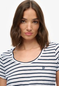 Stribet t-shirt i hvid og marineblå med korte ærmer og rund halsudskæring. Indeholder et lille broderet logo på brystet.