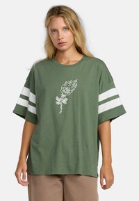 Olijfgroene oversized t-shirt van katoen met witte horizontale strepen op de mouwen. Voorzien van een witte roos en vlammen grafiek op de voorkant.