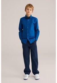 Blå skjorta med knappar, i strukturerad design och långa ärmar, kombinerad med marinblå byxor och vita sneakers. Svart fluga ingår.