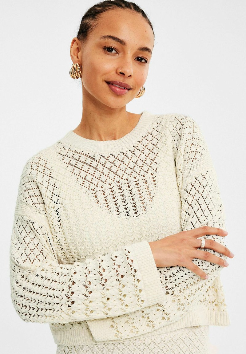Crème kleurige gebreide trui met een los geweven patroon, geribbelde halslijn en mouwen, met een oversized pasvorm en textuurdetails.