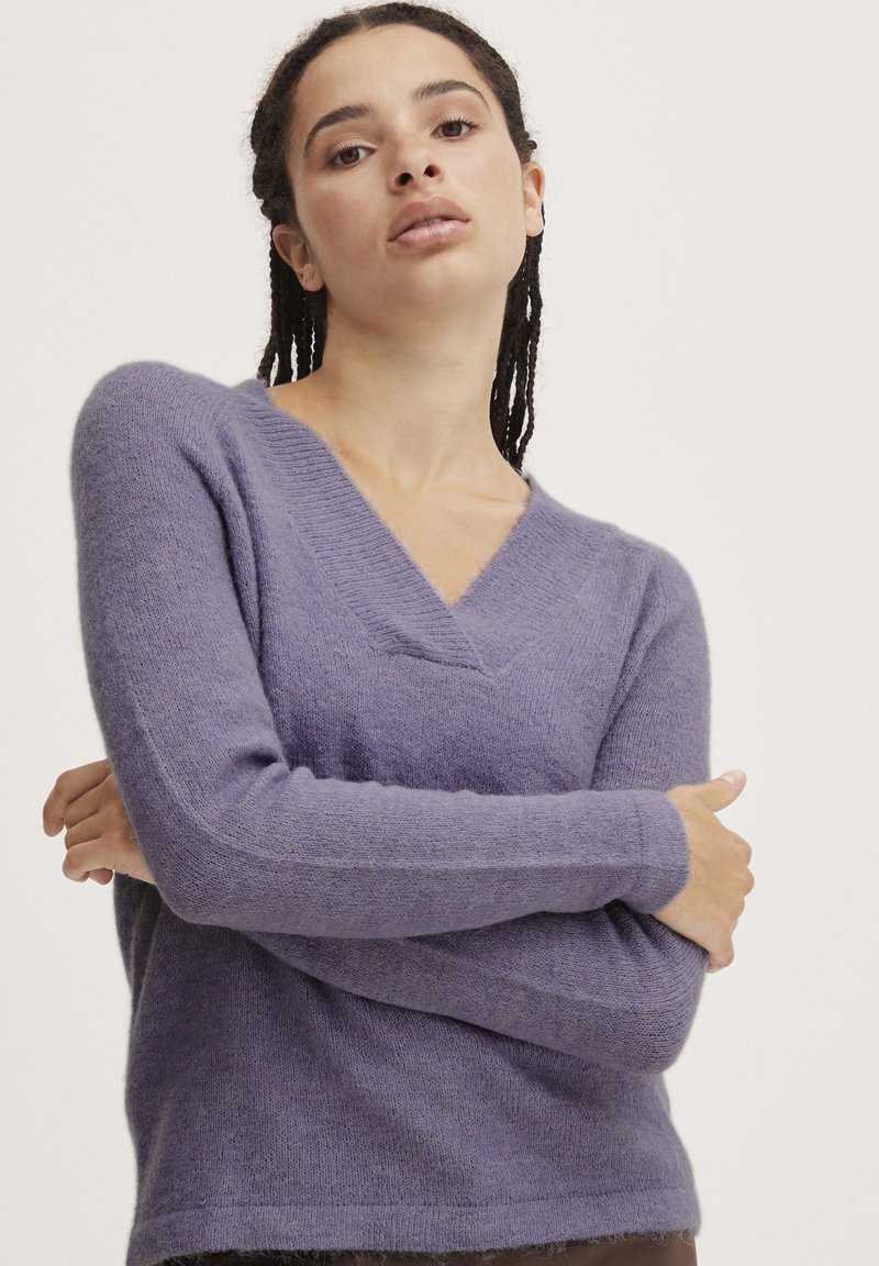 V-hals lilla sweater i blødt, fluffy materiale. Har lange ærmer og en afslappet pasform. Stoffets struktur virker let og varm.