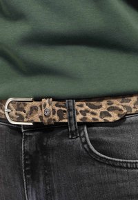 Cintura in suede con stampa leopardata e fibbia argentata indossata con jeans grigio scuro e un top verde in maglia.