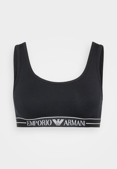 Melna kokvilnas bralette ar apaļu dekoltē, platām siksnām un biezu elastīgu jostu, uz kuras ir balta "Emporio Armani" logo.