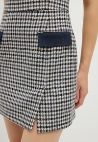 Kostkovaná mini sukně v krémové a námořnické barvě, s potiskem houndstooth, denimovými kapsami a bočním rozparkem pro snadný pohyb.