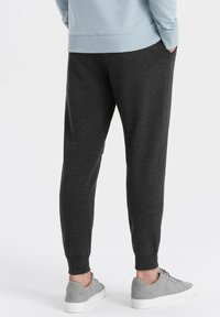 Donkergrijze joggingbroek met taps toelopende pijpen, elastische boorden en zijzakken, gecombineerd met lichtgrijze sneakers. Zachte textuur, casual ontwerp.