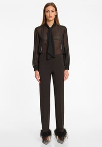 Zwarte sheer blouse met een strik bij de hals, gecombineerd met slim-fit zwarte broeken met bontaccenten bij de enkels. Glanzende zilveren hakken.