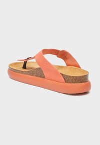 Sandalo in suede corallo con soletta in sughero, ampie cinghie incrociate, tomaia nera e suola spessa in gomma corallo su uno sfondo bianco.