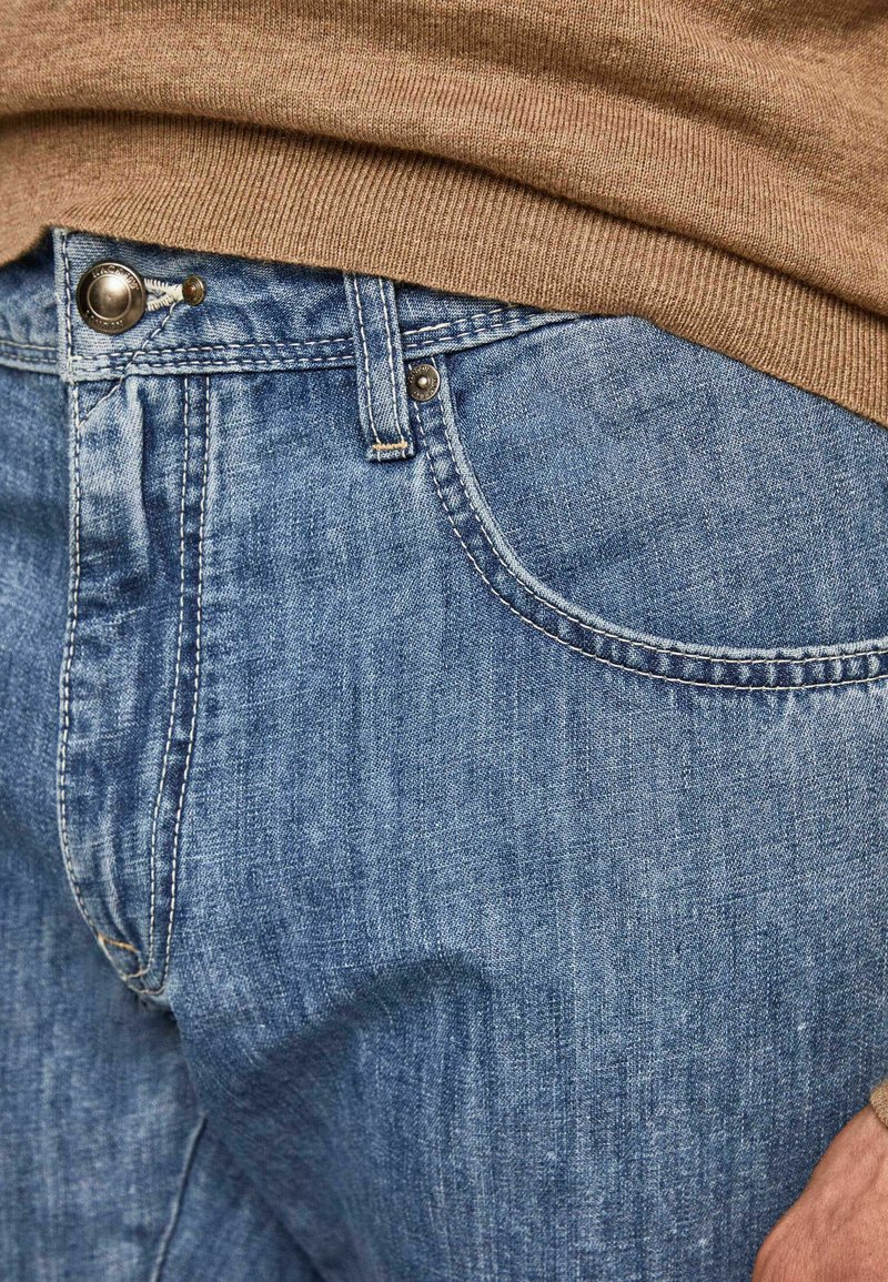 Jeans de mezclilla azul claro con diseño de cinco bolsillos, herrajes de metal en la cintura y una textura ligeramente desgastada.