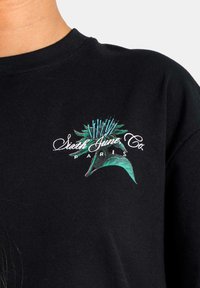 Camiseta de algodón negra con un gráfico floral colorido y el texto "Sixth June Co Paris" debajo, que presenta un cuello redondo y mangas cortas.