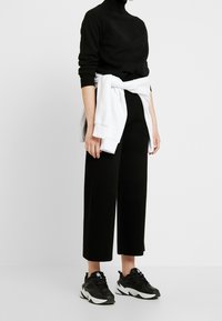 Černý rolák, černé kalhoty širokého střihu a černé tenisky s bílými detaily. Bílá mikina svařená v pase.