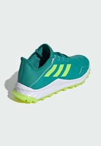 Chaussure de sport teal avec des accents vert fluo, en matériau léger, côtés texturés et semelle intermédiaire blanche. Idéale pour les activités en plein air.