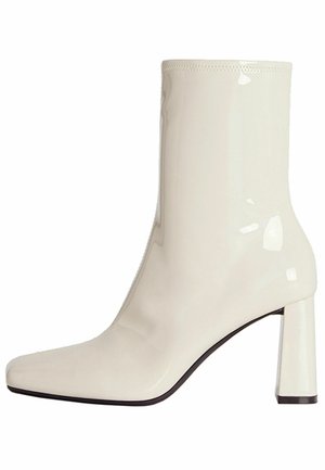 Glanzende witte enkellaars met blokhak en vierkante neus, glad oppervlak en gestikte rand aan de bovenkant.