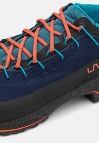 Scarpa blu in suede e mesh con lacci arancioni, suola in gomma nera e dettagli testurizzati per una migliore aderenza. Logo del marchio ben visibile di lato.