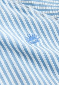 Tessuto a righe blu e bianche con un piccolo sole blu ricamato, texture liscia, materiale leggero e bordi cuciti con cura.