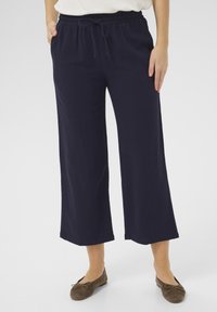 Pantaloni larghi navy con vita elastica e dettaglio con cordoncino, realizzati in tessuto morbido, abbinati a ballerine marroni.