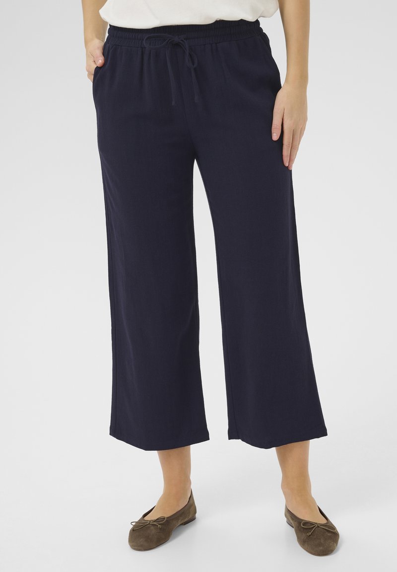 Pantaloni larghi navy con vita elastica e dettaglio con cordoncino, realizzati in tessuto morbido, abbinati a ballerine marroni.