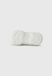 White sneaker sole with textured rubber, featuring zigzag pattern, circular details, and brand markings, designed for traction and durability.