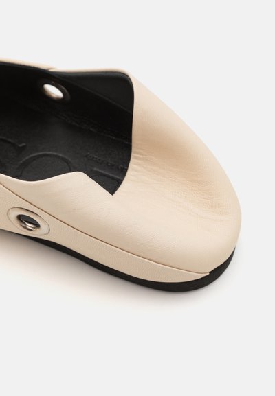 Beige leather shoe with a smooth texture and rounded toe. Features a black inner lining and a silver accent detail on the side.
