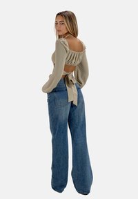 Top corto beige con maniche a sbuffo e dettaglio di laccio sul retro, abbinato a jeans a gamba larga blu chiaro a vita alta. Tessuto morbido e vestibilità rilassata.