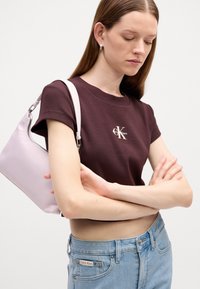 Brązowa bluzka z krótkim rękawem w paski z logo Calvin Klein, jasnoróżowa torebka na ramię oraz jeansy z wysokim stanem w niebieskim kolorze z brandingiem na pasie.
