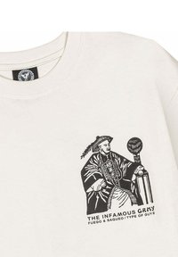 Hellbeige Baumwoll-T-Shirt mit einem schwarzen Grafikdruck eines Mannes in traditioneller Kleidung, darunter mit dem Text "DER INFAME GRMY".