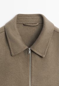 Bruine jas van een wolmix met een kraag en een zilverkleurige rits, met een zachte textuur en een minimalistische stijl.