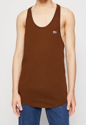 Personne portant un débardeur marron sans manches avec un petit logo « Lee » sur la poitrine, associé à un jean en denim bleu.