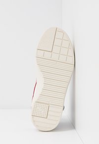 Shoe sole with textured light beige rubber, featuring a grid pattern and support lines. The heel has a slight upward curve and logo detail.