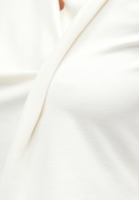 Zbliżenie na miękką, białą tkaninę z widocznymi fałdami i detalami szwów.