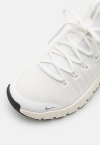 Weiße Sportschuhe mit einer strukturierten Oberseite, dünnen Schnürsenkeln und einer schwarzen Gummisohle. Verfügt über ein Logo in der Nähe der Zehe und ein schlankes Design.