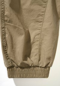 Pantalones caqui con puños elásticos, fabricados en tela ligera. Presentan una textura suave y detalles de costura en las costuras laterales.