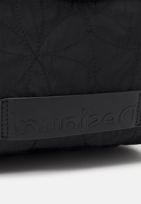 Czarna pikowana torba z teksturowanym wzorem, gładkim skórzanym paskiem z wytłoczonym logo oraz subtelnie ozdobnymi szwami.