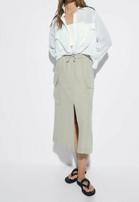 Let skinnende, hvid, button-up skjorte over en beige linned nederdel med en front-slids og sidelommer. Sorte sandaler fuldender outfittet.