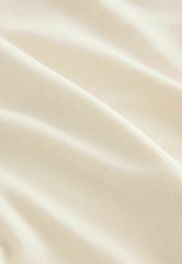 Tissu beige, lisse avec un léger éclat, présentant une texture à fines côtes et une drape douce, créant des plis et contours délicats.