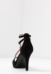 Czarne zamszowe szpilki z paskiem na kostce, otwartym noskiem i stożkowym obcasem, charakteryzujące się gładką teksturą i minimalistycznym designem.