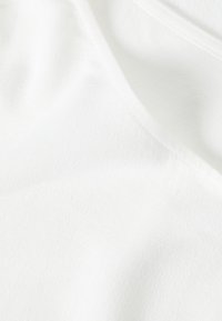 Biely textil s jemným vzorom rybej kosti, hladká textura a splývavý dizajn, ktorý vystihuje jemné prešitie na okrajoch.