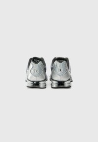 Silver athletic shoes featuring a mesh upper and cushioned sole, with distinct heel structure and black accents. Back view.