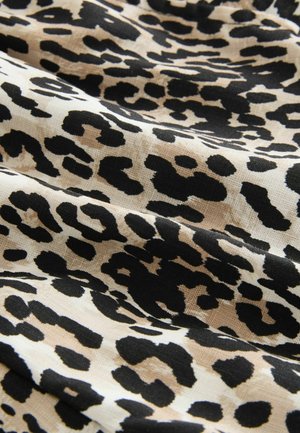 Løveprint stof med en beige baggrund og kraftige sorte pletter. Teksturen ser glat og let krøllet ud.