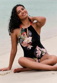 Musta kukallinen yksiosainen uimapuku, jossa punaiset olkaimet ja avainreikäyksityiskohta. Sisältää sekoituksen vaaleanpunaisia, valkoisia ja vihreitä kukkakuoseja sileällä kankaalla.