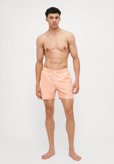 Ferskenbadshorts laget av lett stoff, med elastisk liv med snøring, og en liten hvit logoaksent.