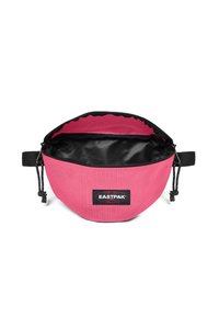Vaaleanpunainen kangaspussi, jossa on musta sisus, säädettävä nyöri ja Eastpak-logo etuosassa. Pyöreä muoto kompaktiin säilytykseen.