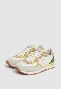 Zapatillas con un diseño en capas, en tonos beige claro, con acentos amarillos y verdes, fabricadas en material de ante y malla, con cordones blancos y una suela de goma.
