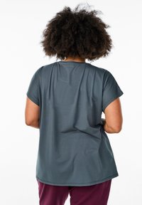 T-shirt grigio a maniche corte con una vestibilità rilassata, texture liscia, scollatura rotonda e orlo posteriore leggermente più lungo. Indossato con pantaloni bordeaux.