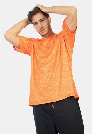 Camiseta atlética de manga corta de un brillante color naranja, con un patrón texturizado, combinada con pantalones negros y un detalle de cuerda roja.