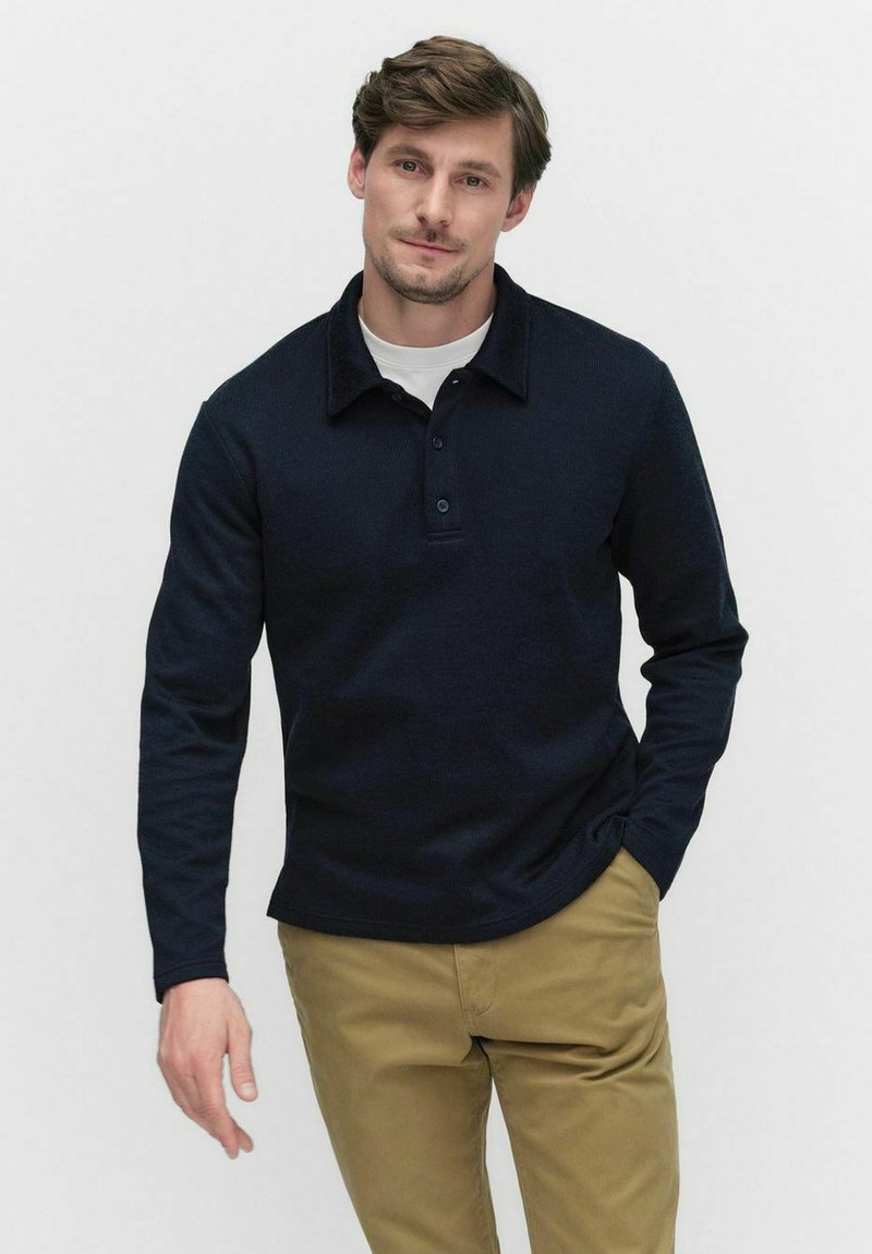 Navy långärmad polo i texturerad stickad tyg med krage, tre knappar och en avslappnad passform, kombinerad med khaki byxor.