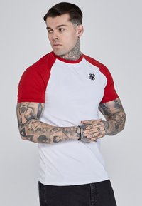 Valge T-särk punaste raglanvarrukatega, millel on rindkeres väike must logo. Pehme puuvillane kangas ja sobiv disain.