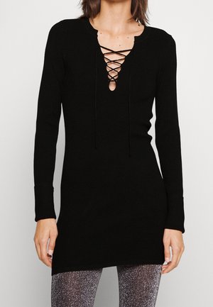 Musta neulemekko, jossa on nauhakuja, pitkät hihat ja ribbitekstuuri, yhdistettynä kimalteleviin leggingsiihin.